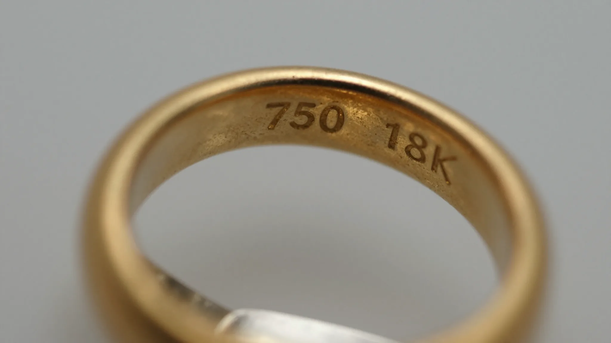 Close-up macro photograph of 18k gold hallmark stamp on antique gold ring band, neutral studio lighting