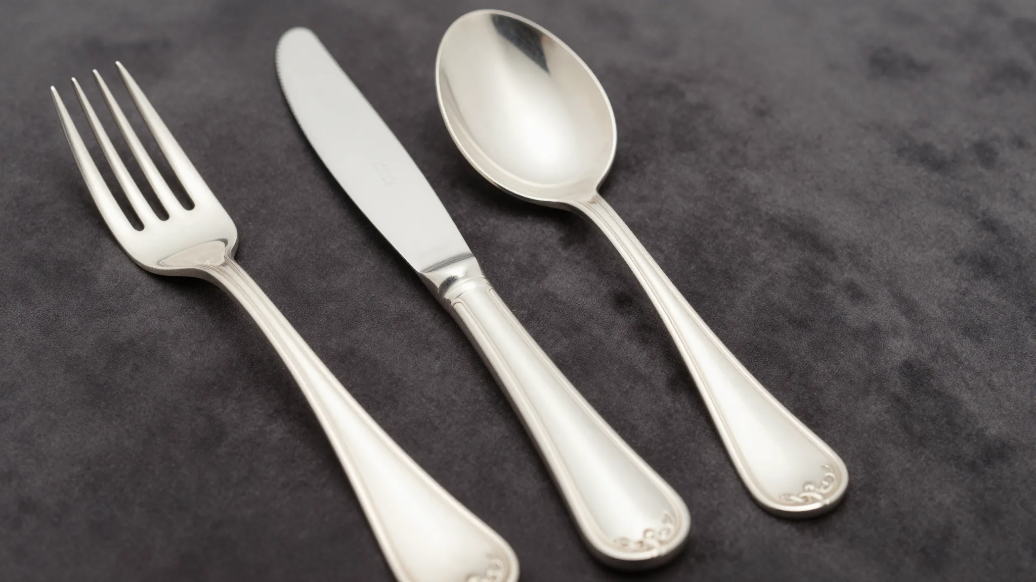Tiffany R Pattern sterling silver flatware set arranged on dark velvet with hallmark detail visible